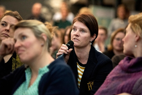 Vrouw met microfoon neemt het woord tijdens bijeenkomst.