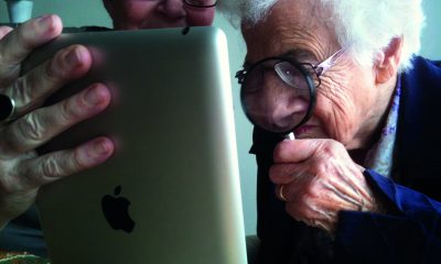 Twee oudere vrouwen bekijken een ipad; een ervan gebruikt een vergrootglas