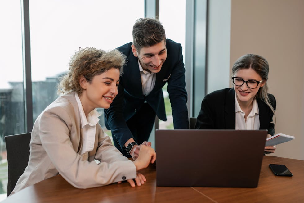 Drie collega's overleggen voor een laptop in een kantoor.