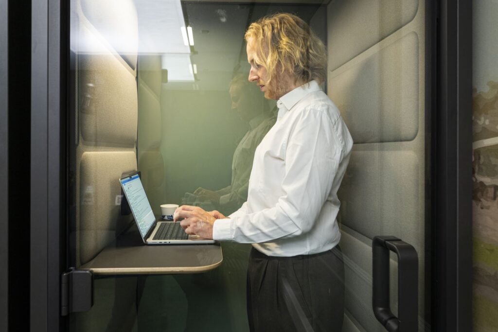Iemand staat achter diens laptop in een afgesloten hokje in een kantoor.