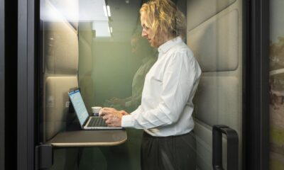 Iemand staat achter diens laptop in een afgesloten hokje in een kantoor.